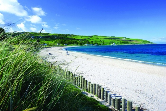The sandy curve of Cushendun Beach with green Glens of Antrim hills behind