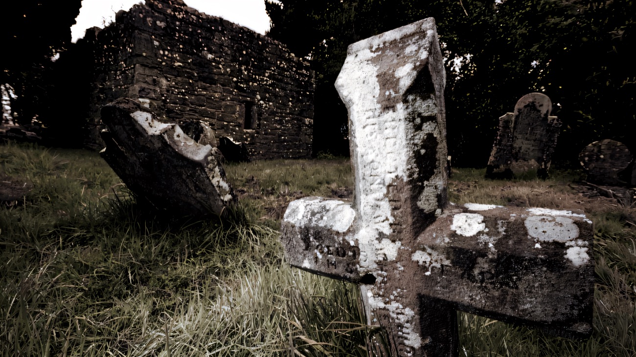 A weathered, lichen-crusted stone cross standing before the ruined walls