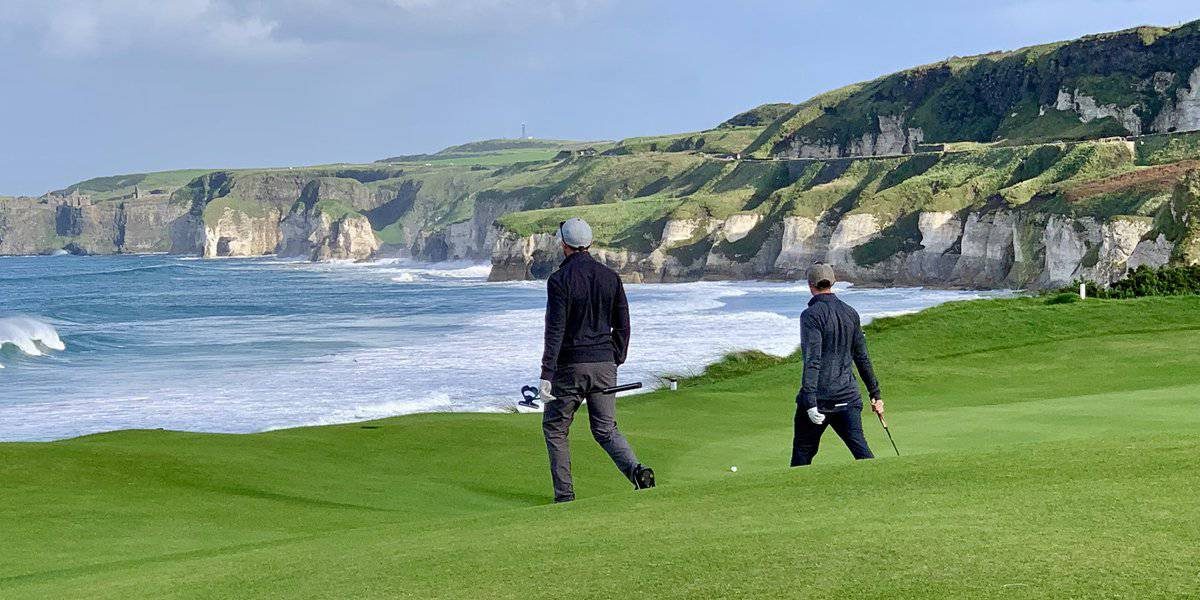Golfers walking the fairway at Royal Portrush with the White Rocks cliffs and sea behind