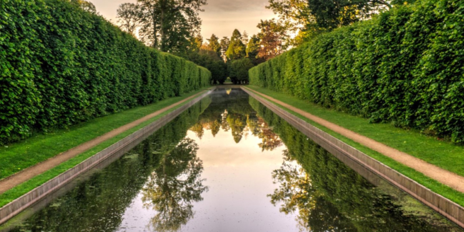The long ornamental canal at Antrim Castle Gardens, flanked by tall clipped hedges, mirror-still at golden hour