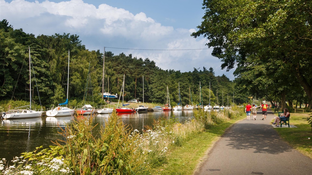 A path running beside a line of moored yachts at Antrim Lough Shore Park on a summer day