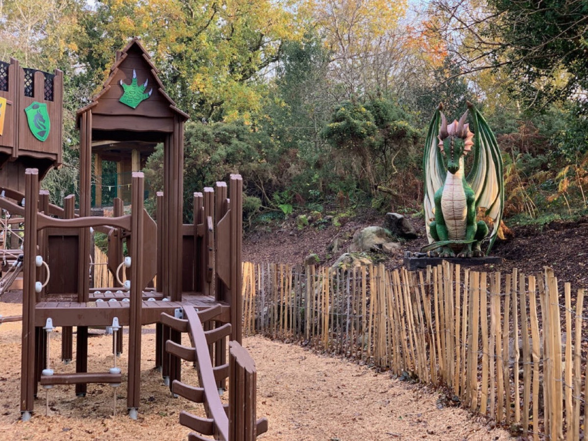 A wooden castle-themed adventure playground beside a green dragon model in the Dragons Den play area