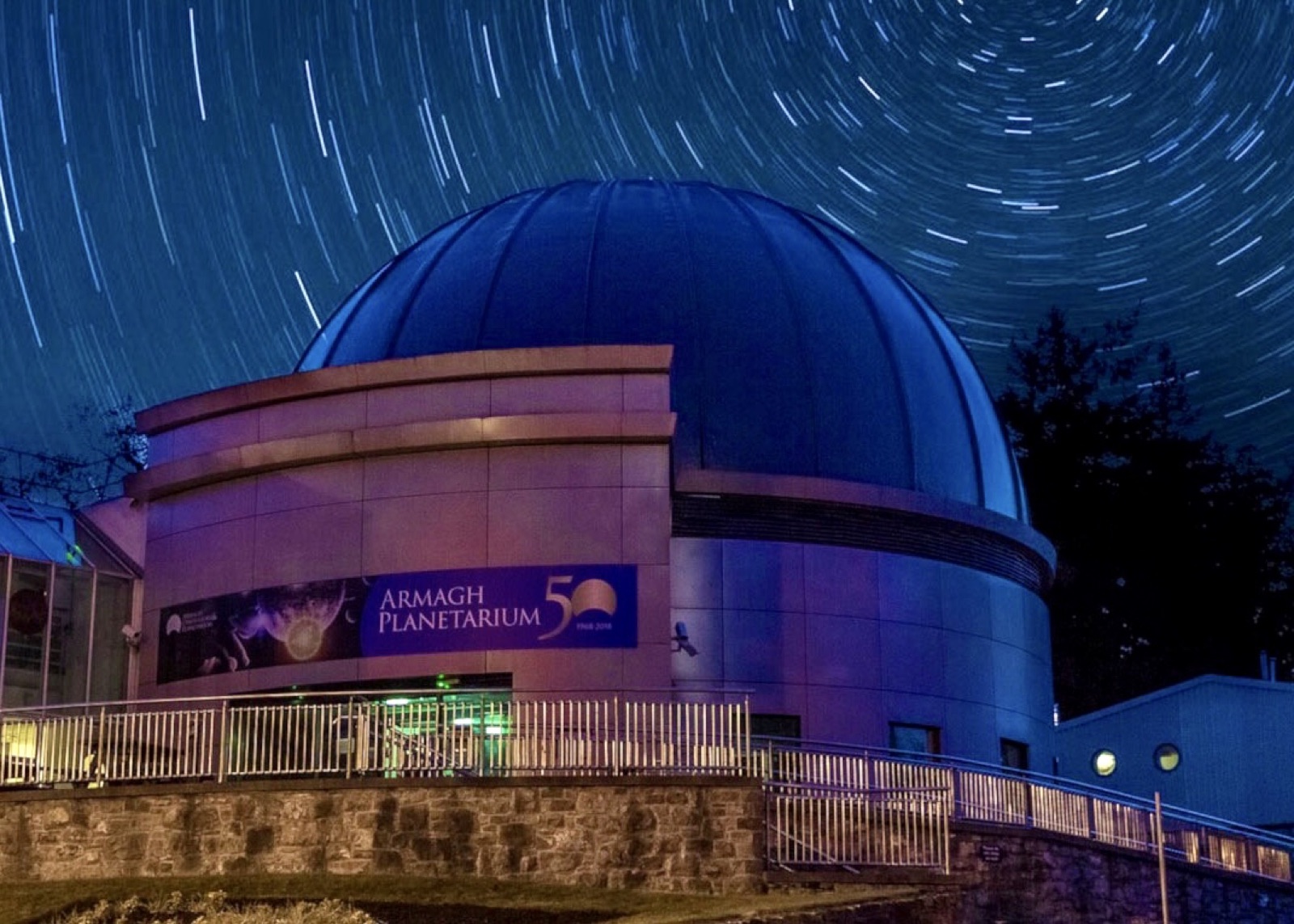 The domed planetarium building at night under a sky of star-trails