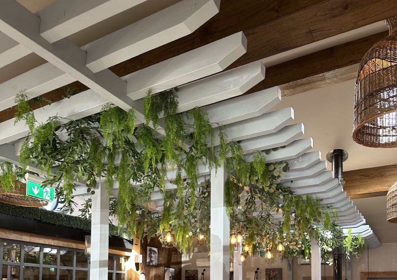 Inside the Ashvale tea room: pale beams hung with trailing greenery and warm pendant bulbs