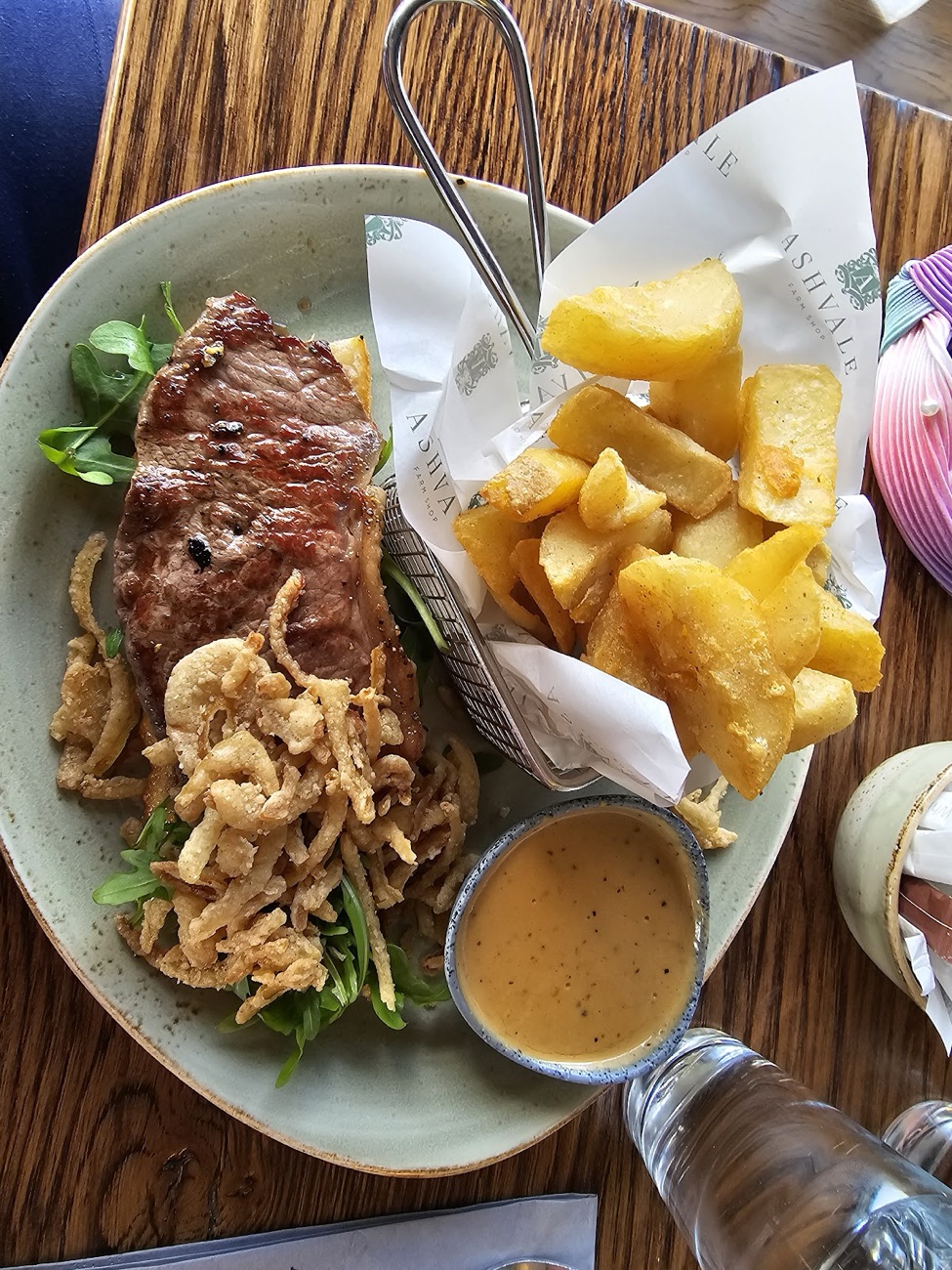 A steak with chunky chips in a basket lined with Ashvale Farm Shop paper
