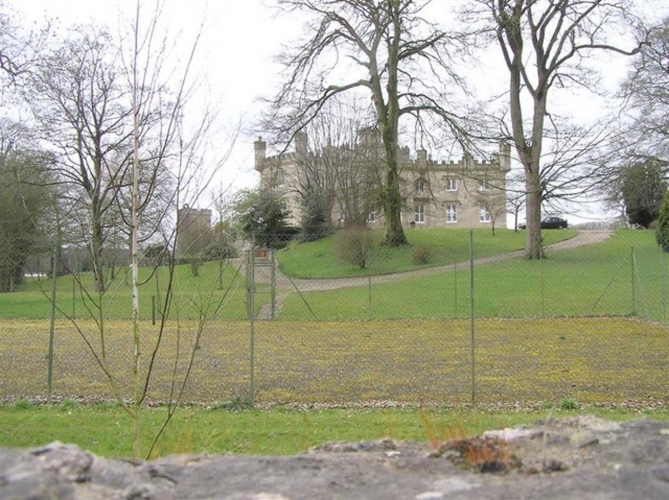 Augher Castle seen across a field from beyond the boundary fence, framed by mature trees