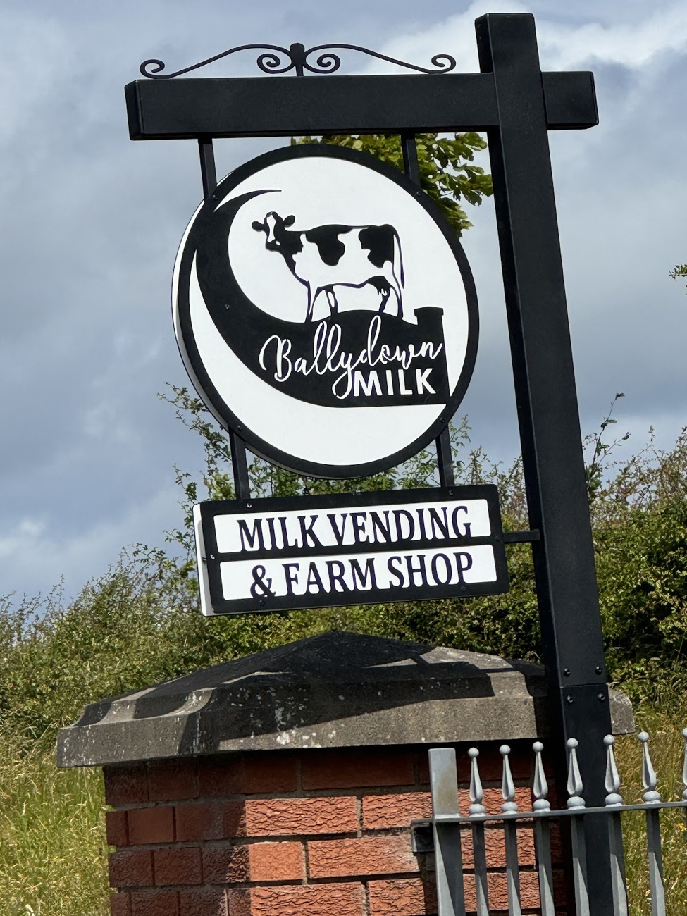 The hanging Ballydown Milk sign reading Milk Vending and Farm Shop on a brick pillar at the roadside