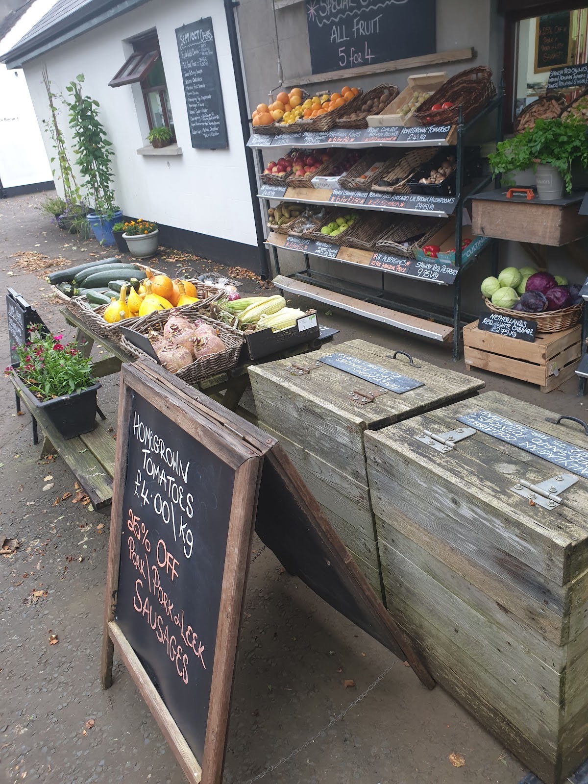 Vegetables in wicker baskets and wooden crates outside the whitewashed Ballylagan farm shop, chalkboards listing prices