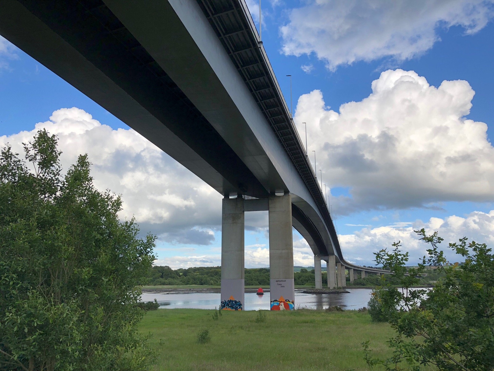 The underside of the Foyle Bridge arching over Bay Road Park with the river and blue sky beyond
