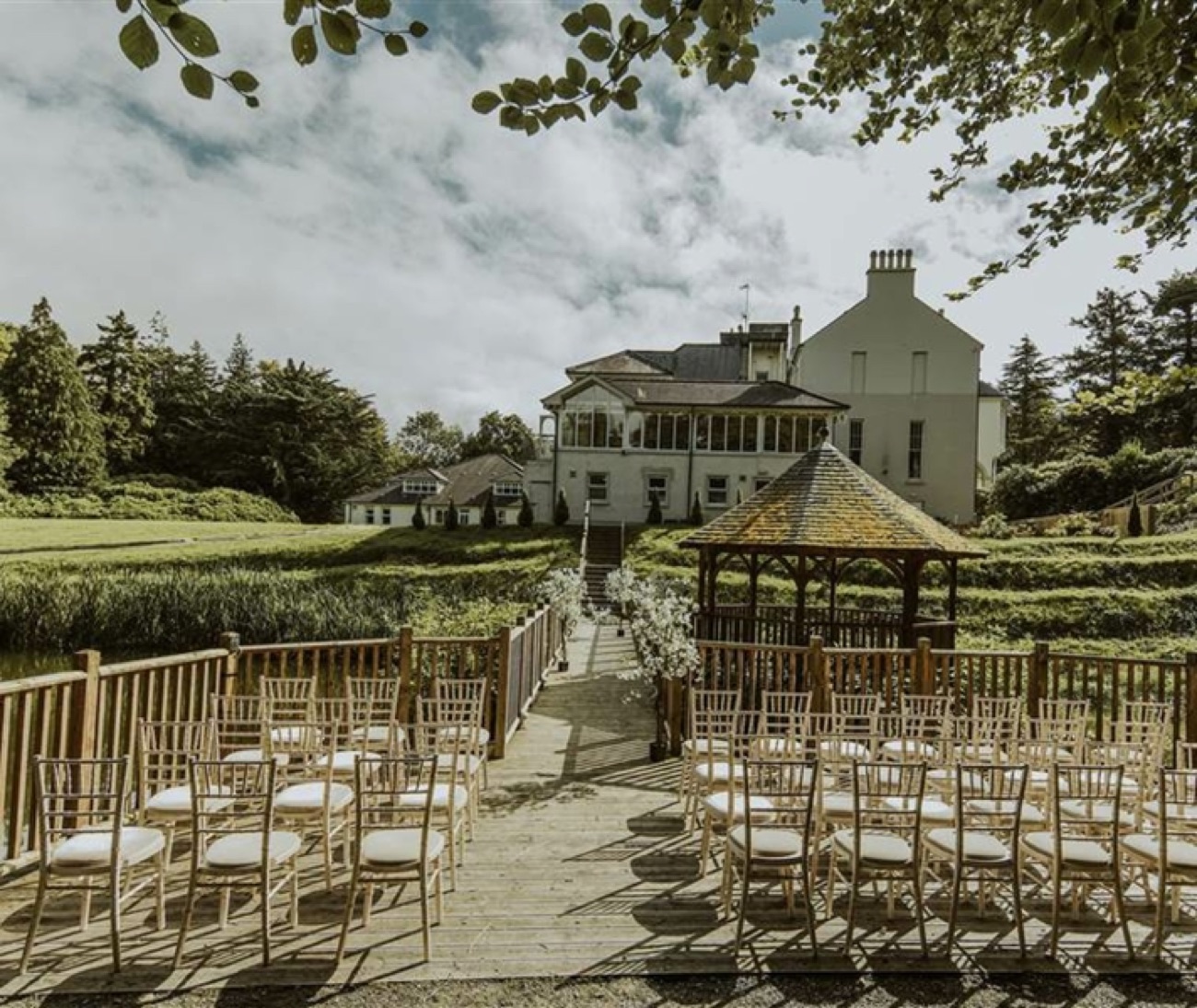 A wooden boardwalk and gazebo set out over the water in the grounds of Beech Hill, with the house rising behind