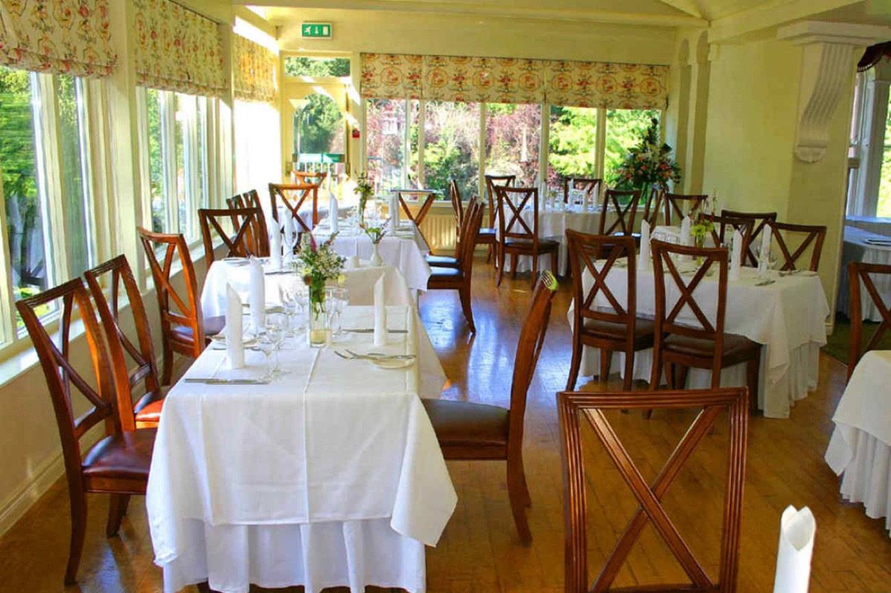 A bright conservatory dining room at Beech Hill, tables laid in white linen with windows looking out over the gardens