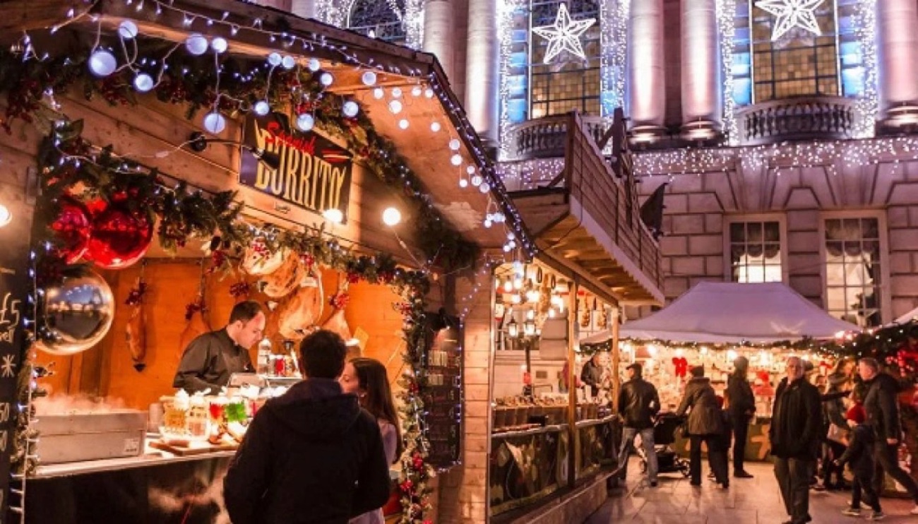 A festive food chalet strung with lights at the Belfast Christmas Market with City Hall lit up behind