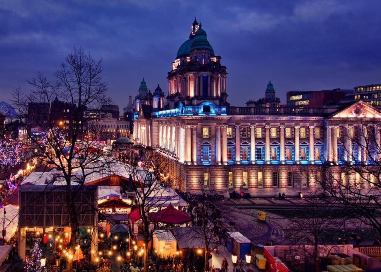 An elevated view of the whole Belfast Christmas Market lit up at dusk with City Hall floodlit above the stalls