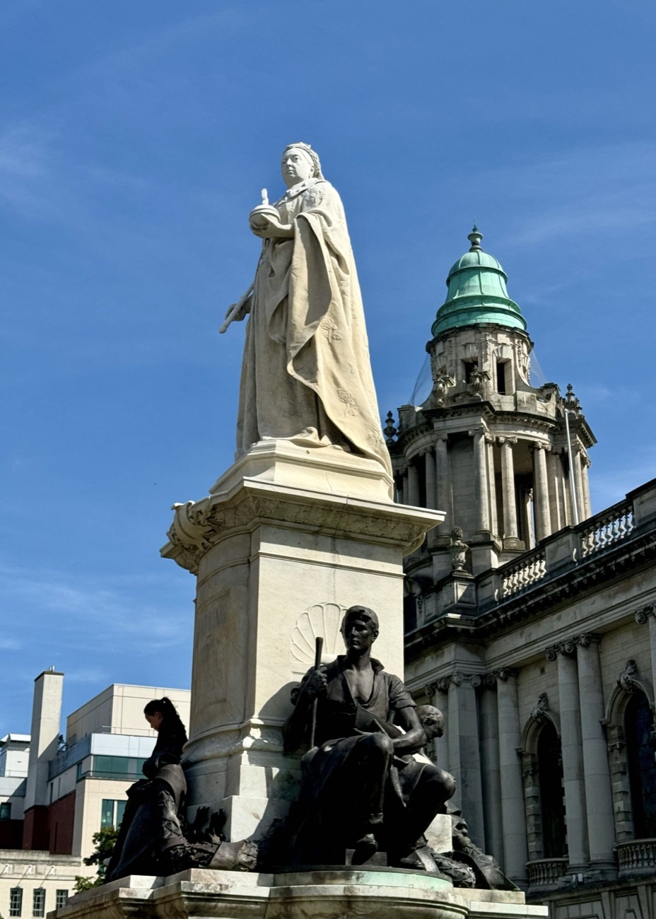 The white marble Queen Victoria statue in the grounds of Belfast City Hall with a green copper dome behind