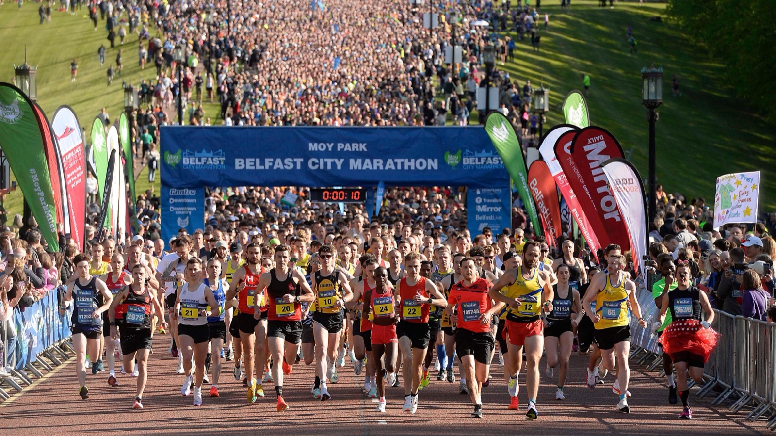 A mass of runners surging from the start line under the Belfast City Marathon banner at Stormont