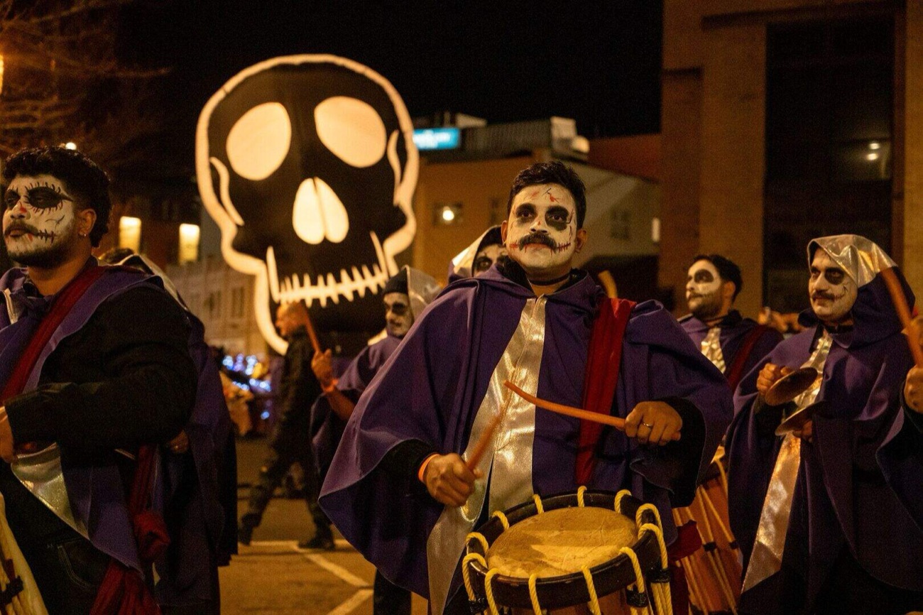 Carnival drummers in purple capes and skull face-paint with a giant skull banner at a Halloween parade
