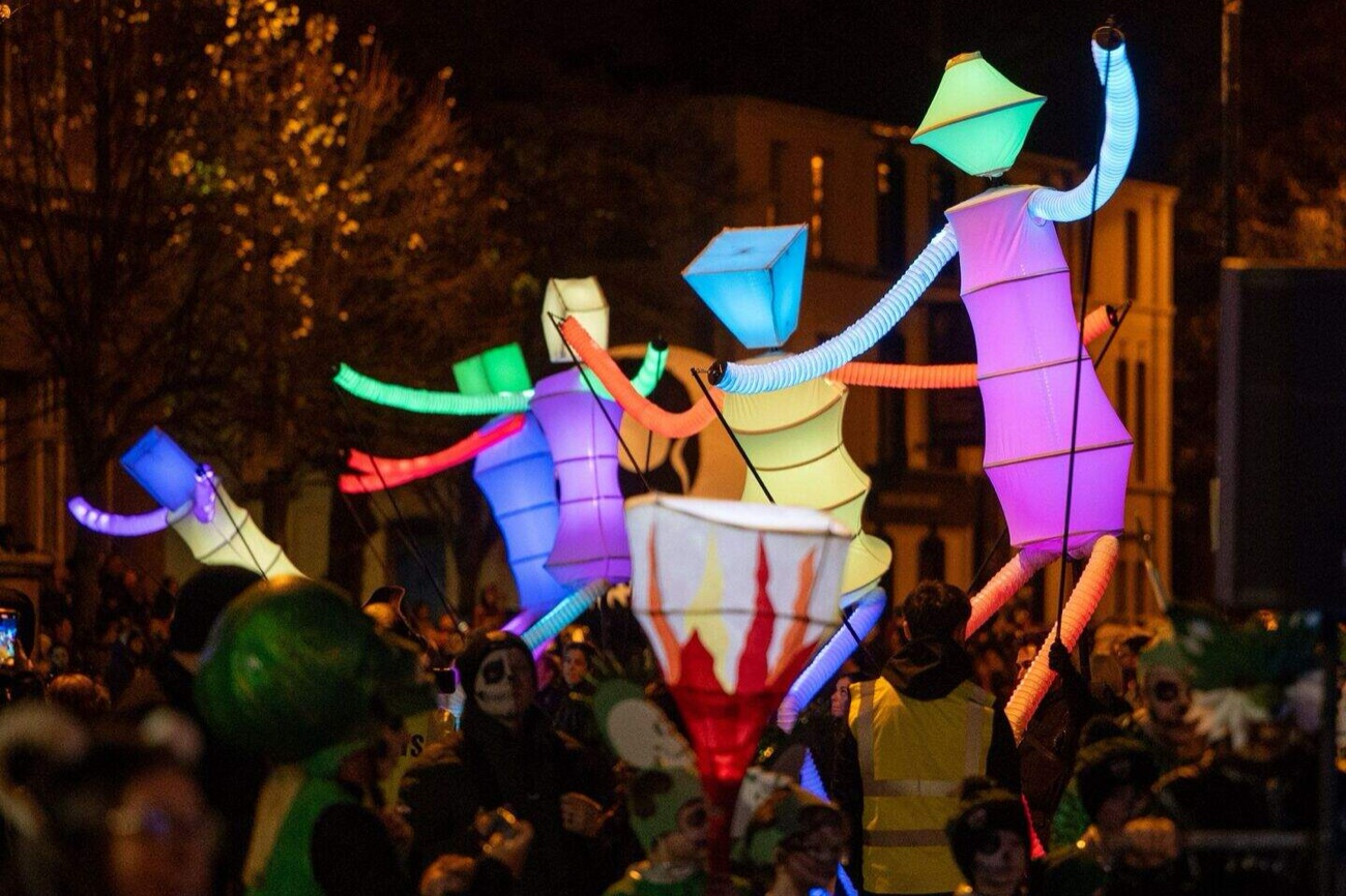Glowing illuminated lantern puppets carried above the crowd at a Belfast Halloween carnival at night
