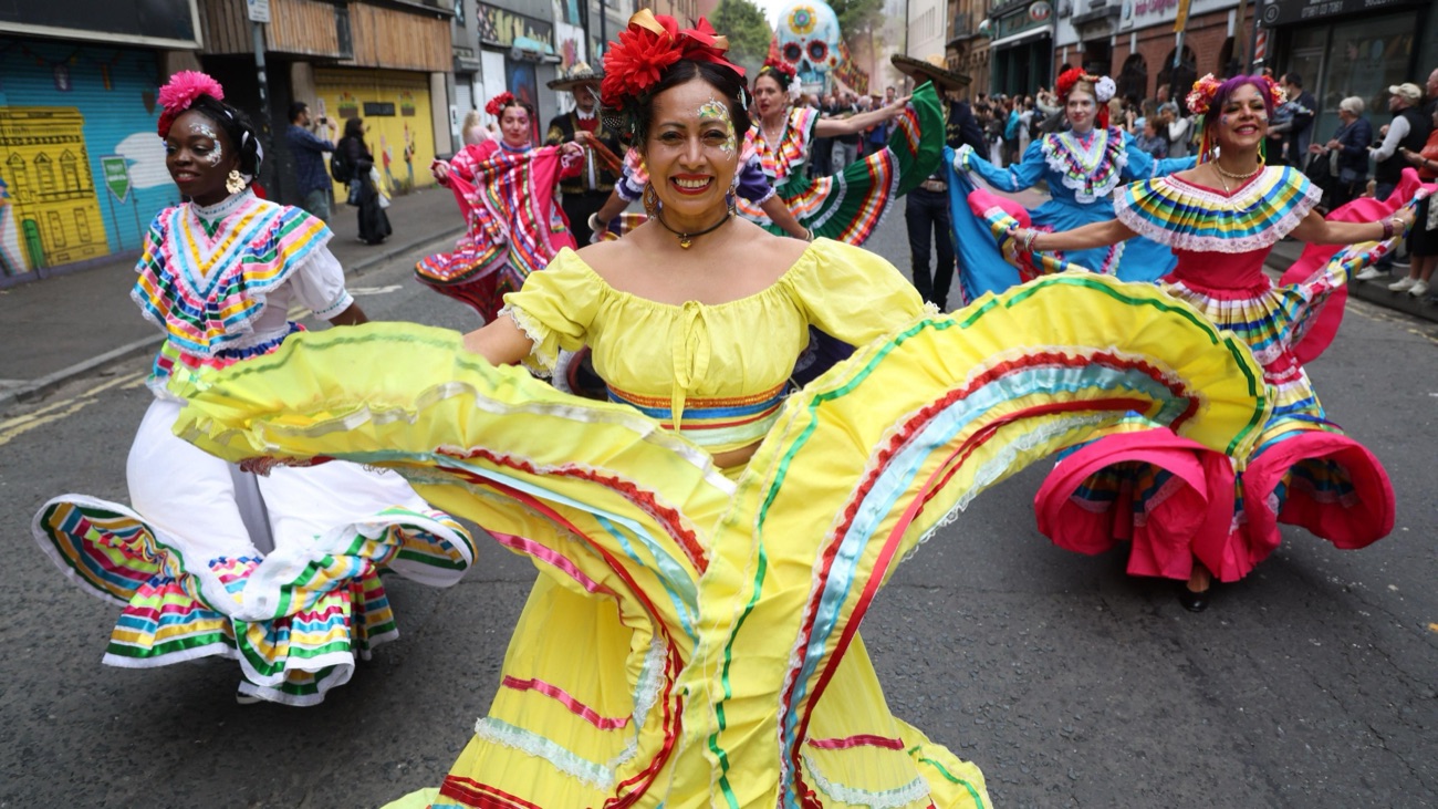Latin American folk dancers in bright yellow and pink ruffled dresses spinning at Belfast Mela