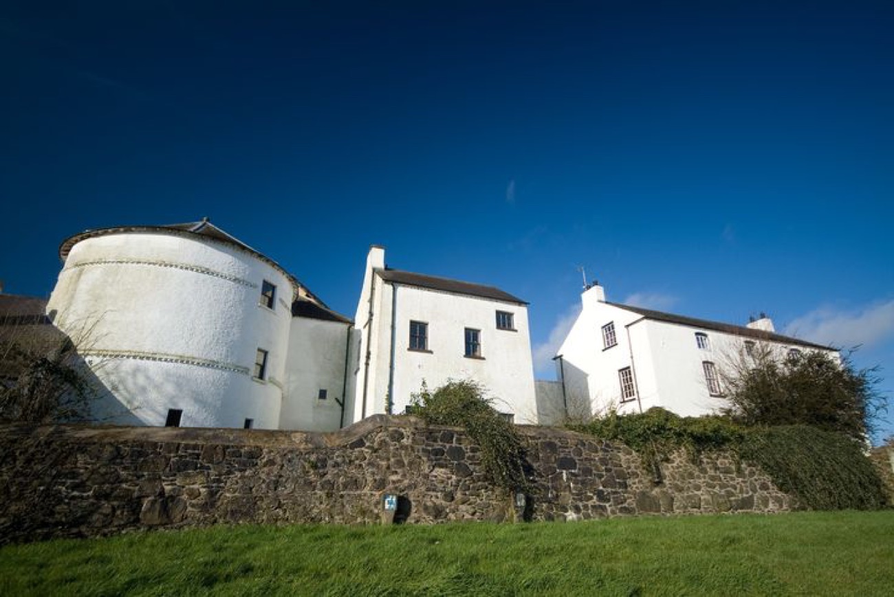 The round flanker tower and fortified house at Bellaghy Bawn seen over the old stone wall against a blue sky
