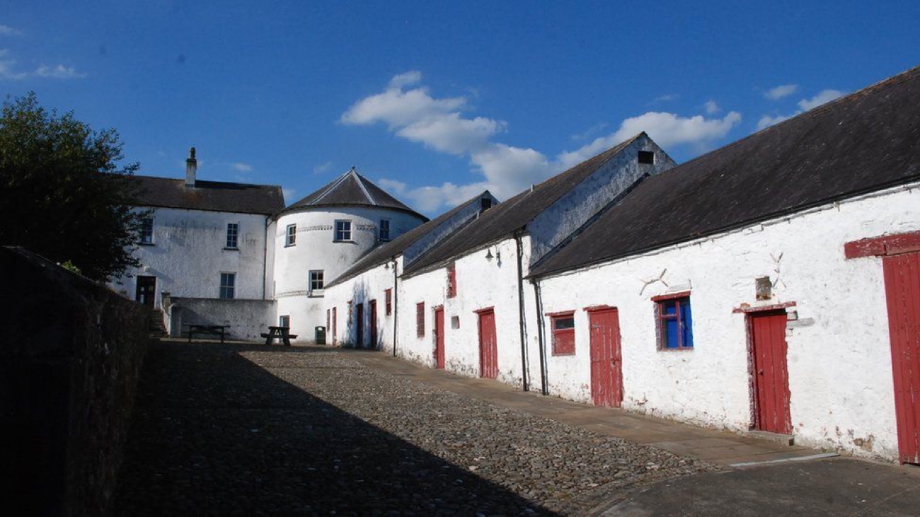 The cobbled courtyard lane at Bellaghy Bawn, red-doored outbuildings on the right and the round tower behind
