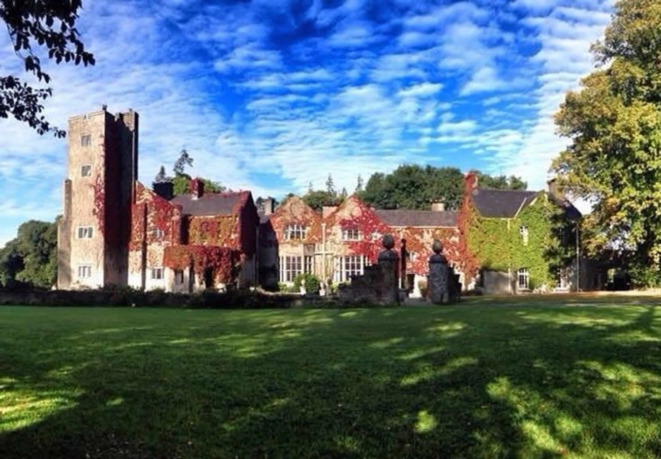 Belle Isle Castle under a blue sky, its walls turning red with autumn ivy, statues on the lawn