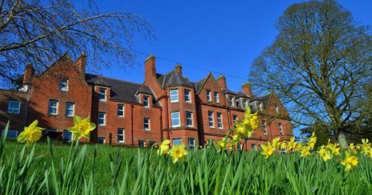The red-brick Servite Priory building at Benburb behind a bank of daffodils under a blue sky