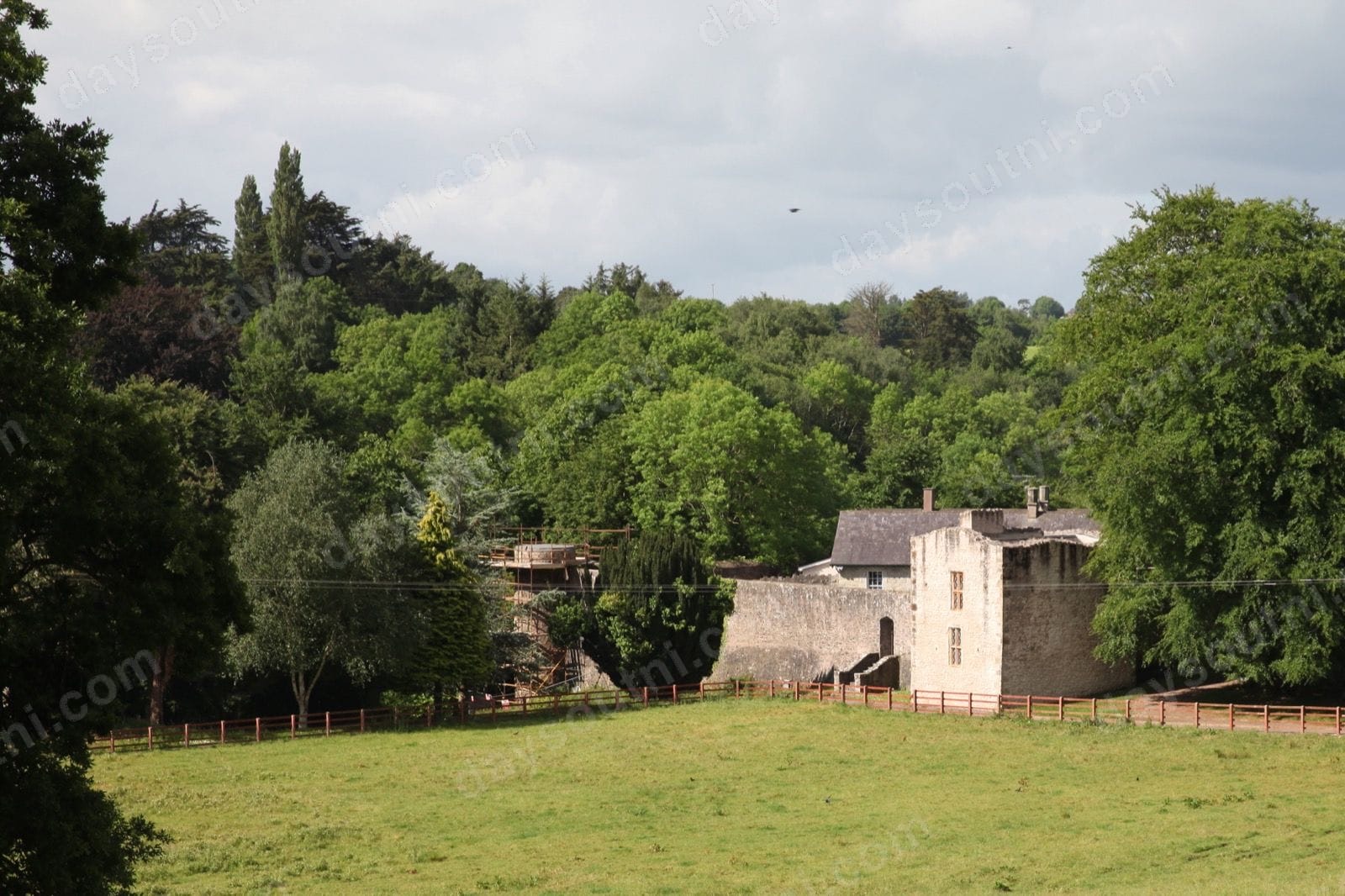 Benburb Castle's grey bawn walls and tower on the wooded valley slope above the River Blackwater, with a green field in front