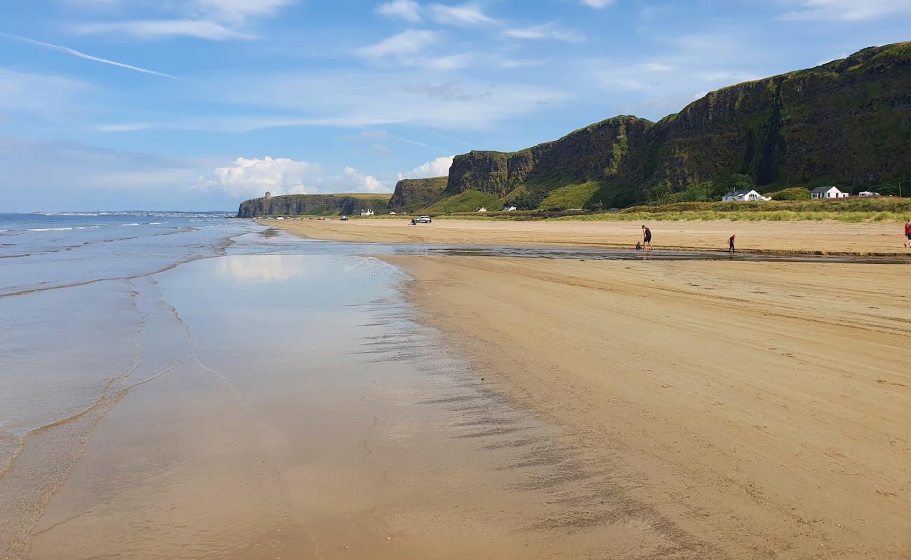 The wet firm sand of Benone Strand reflecting the sky with the green Binevenagh cliffs rising behind