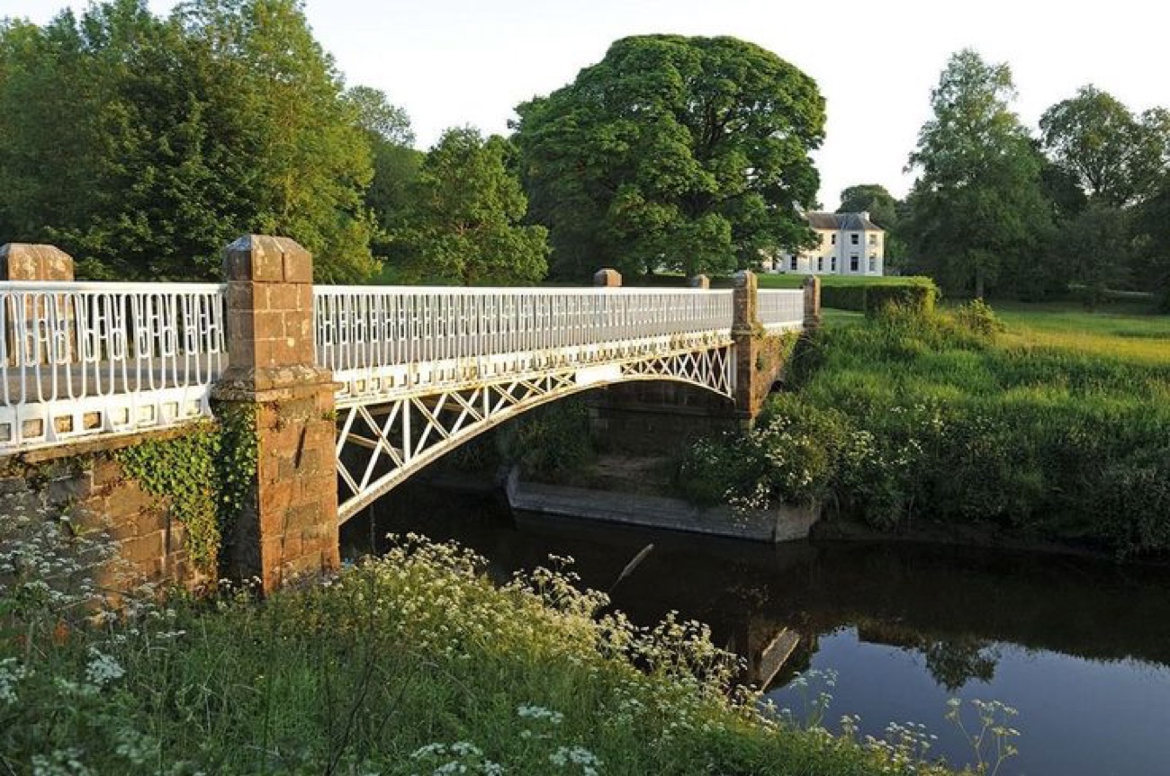 The white iron bridge over the River Bush with the house beyond