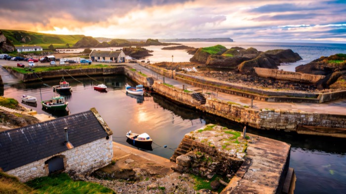 Boats moored in Ballintoy Harbour at sunset with sea stacks beyond
