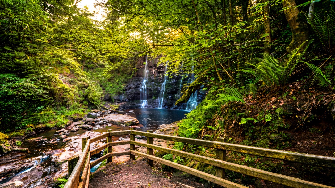 A wooden walkway leading to a double waterfall pouring into a dark pool at Glenariff