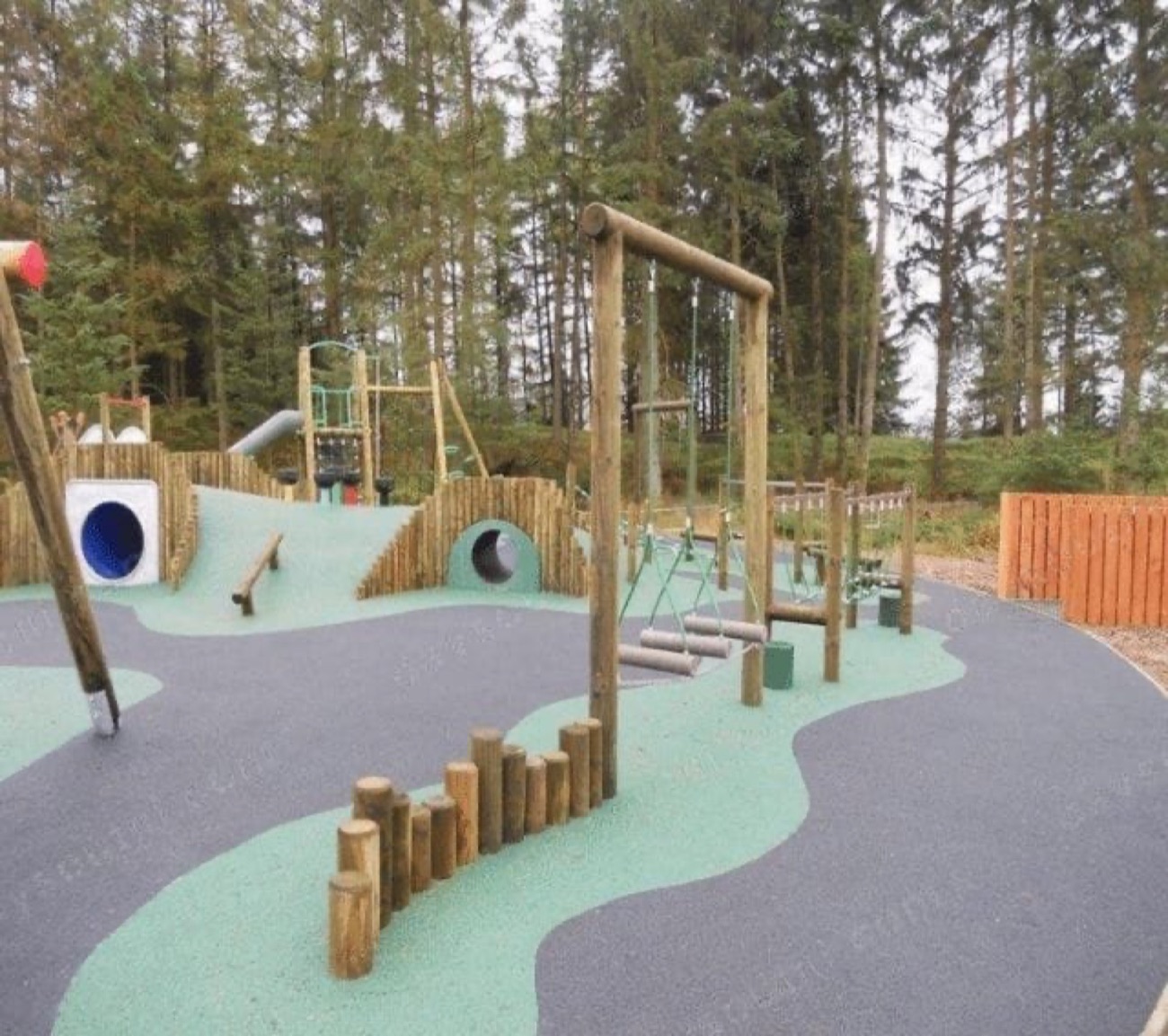 Timber climbing frames and swings of the forest play park at Davagh among tall conifers