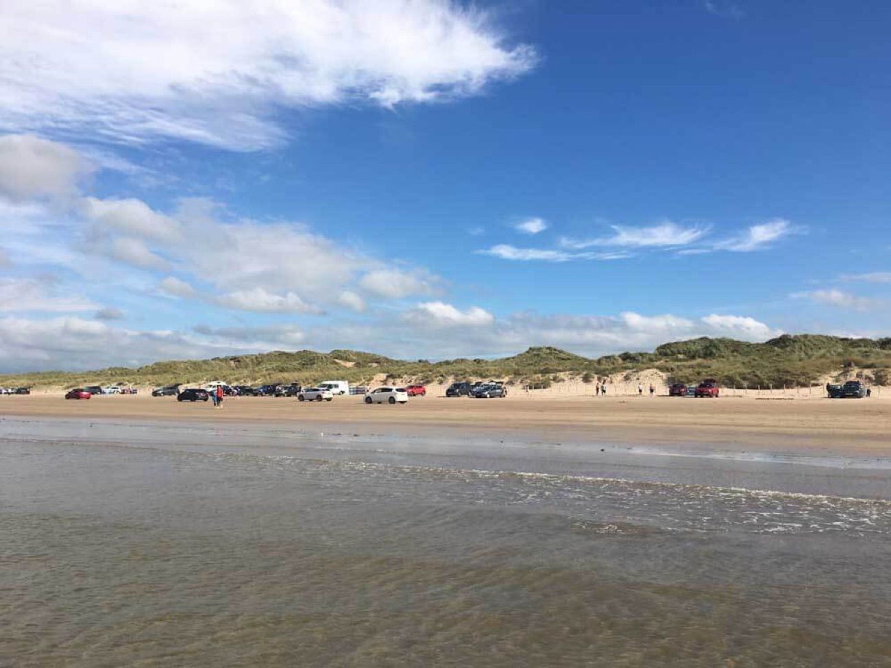 Cars parked along the golden sand of Portstewart Strand under a blue summer sky