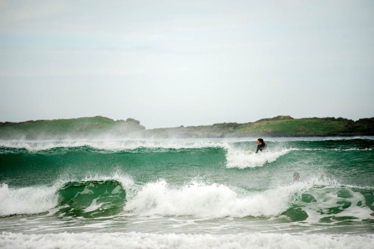 A surfer riding a clean green wave at Whiterocks Beach with the headland behind