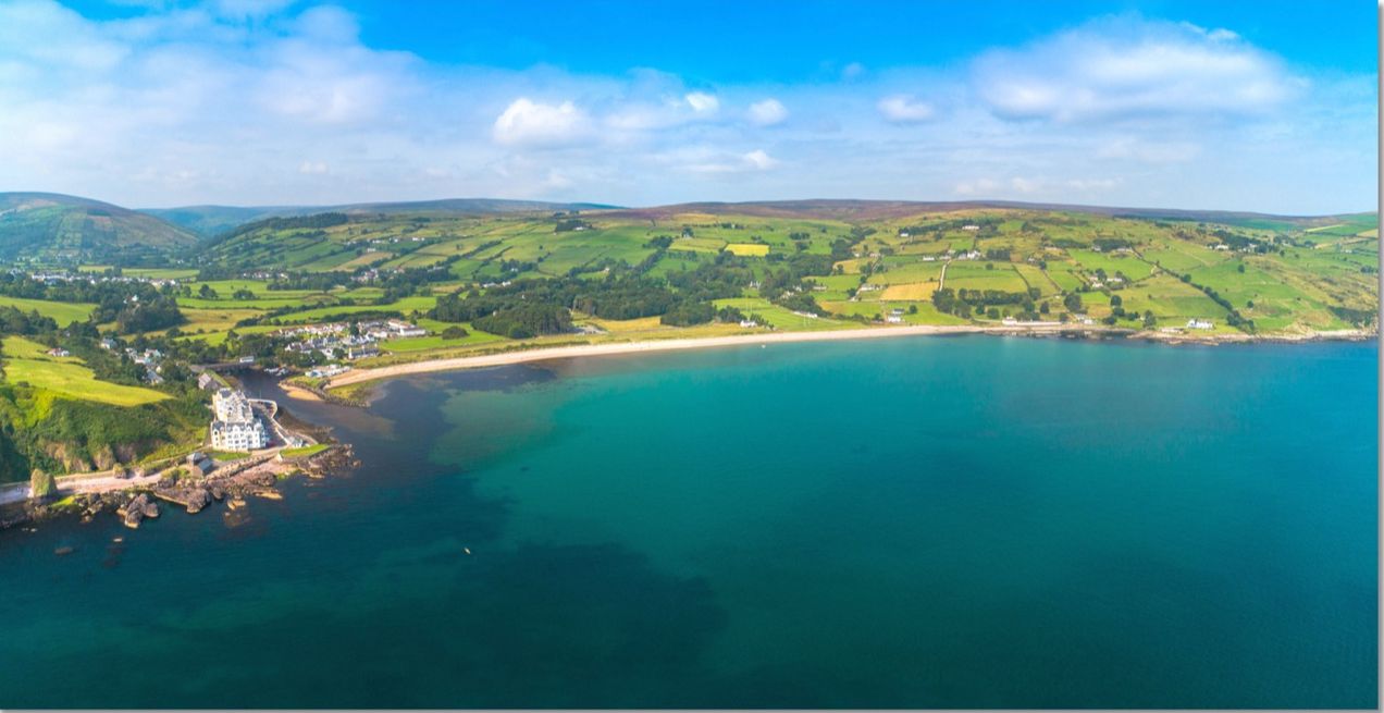 Aerial view of the sheltered turquoise bay and sandy beach at Cushendun in the Glens of Antrim