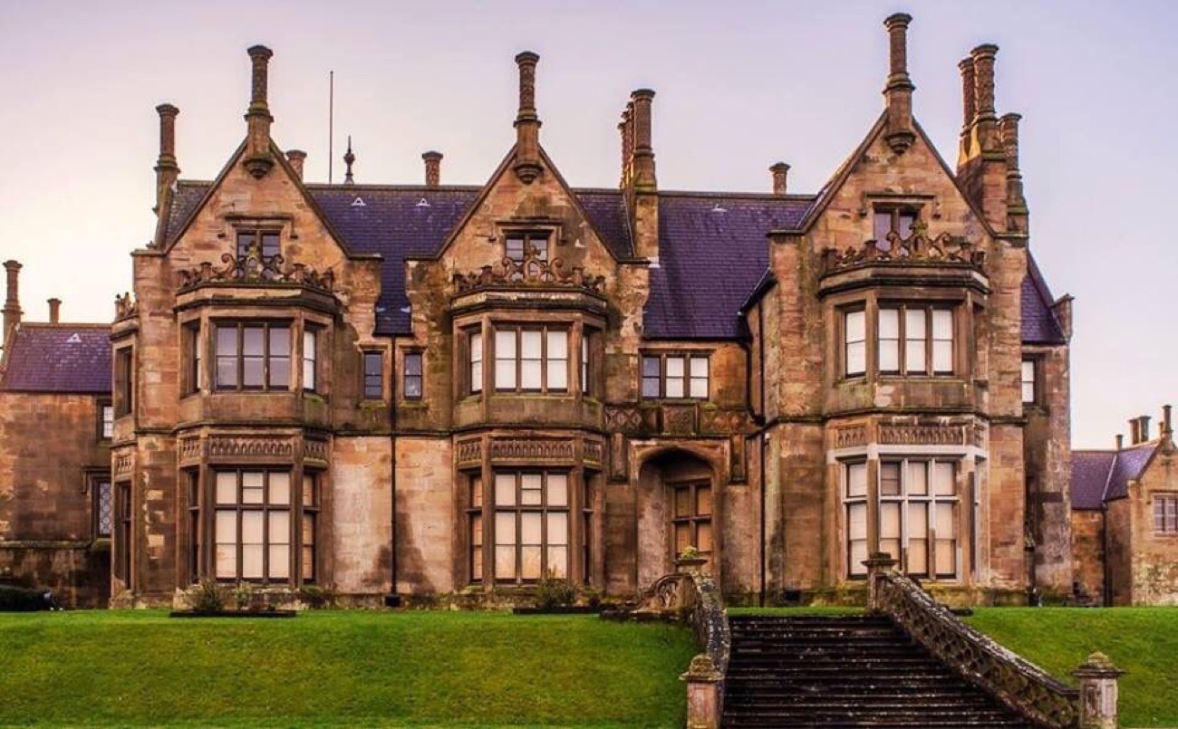 The ornate Elizabethan-style facade of Brownlow House with twin bay windows and a stone staircase up to the lawn