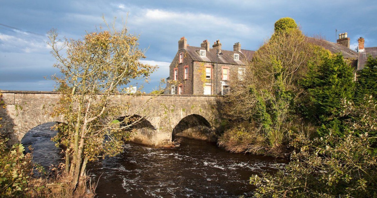 A stone bridge over the River Bush running through Bushmills village, with terraced houses on the far bank in autumn light