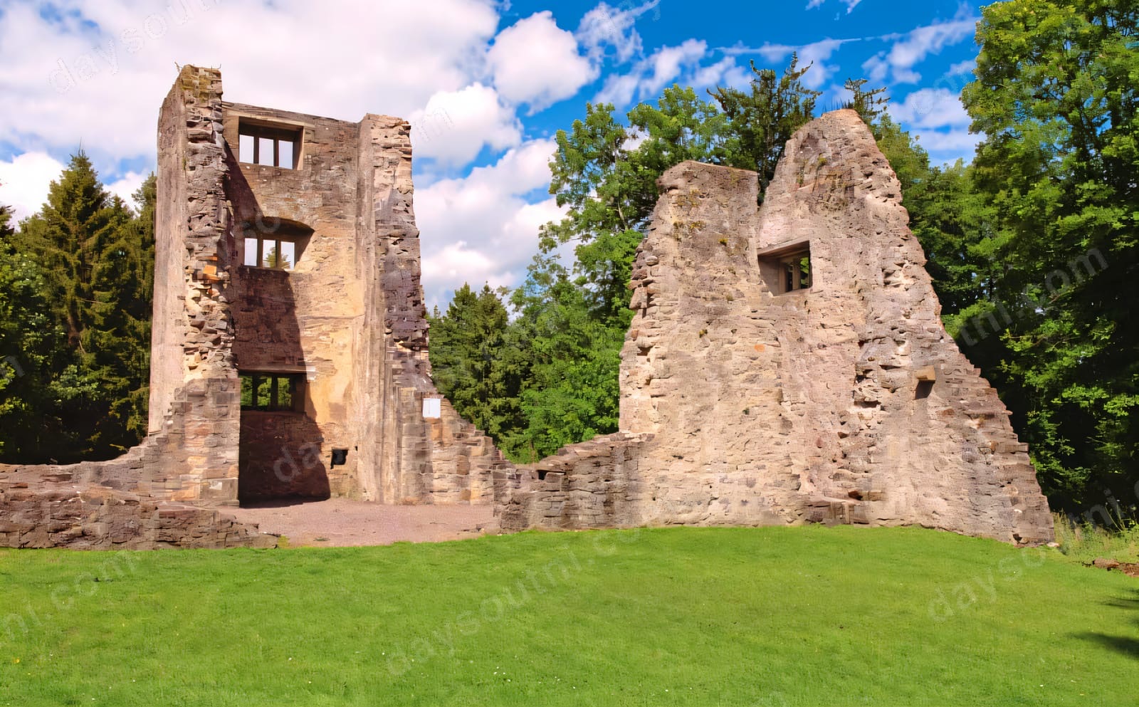 The ruins of Old Castle Archdale, two tall stone gable walls standing on a green lawn edged by tall trees under a blue sky