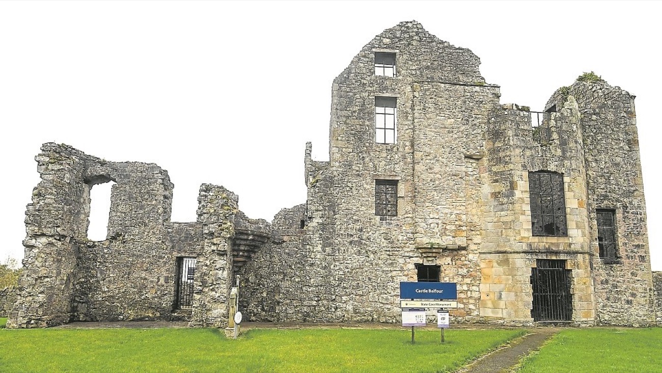 The tall ruined facade of Castle Balfour with its empty stone windows and the State Care monument sign at its foot