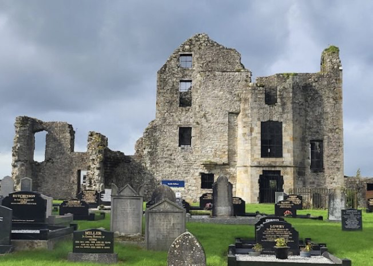 Castle Balfour rising behind the headstones of Holy Trinity churchyard under a moody Fermanagh sky