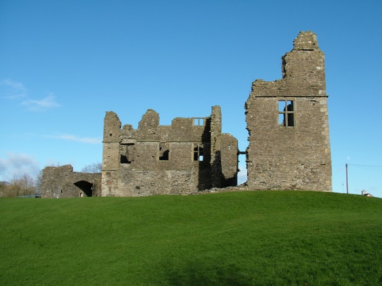 The ruined Jacobean manor house of Castle Caulfield standing on its green mound under a blue sky, with the gatehouse arch to the left