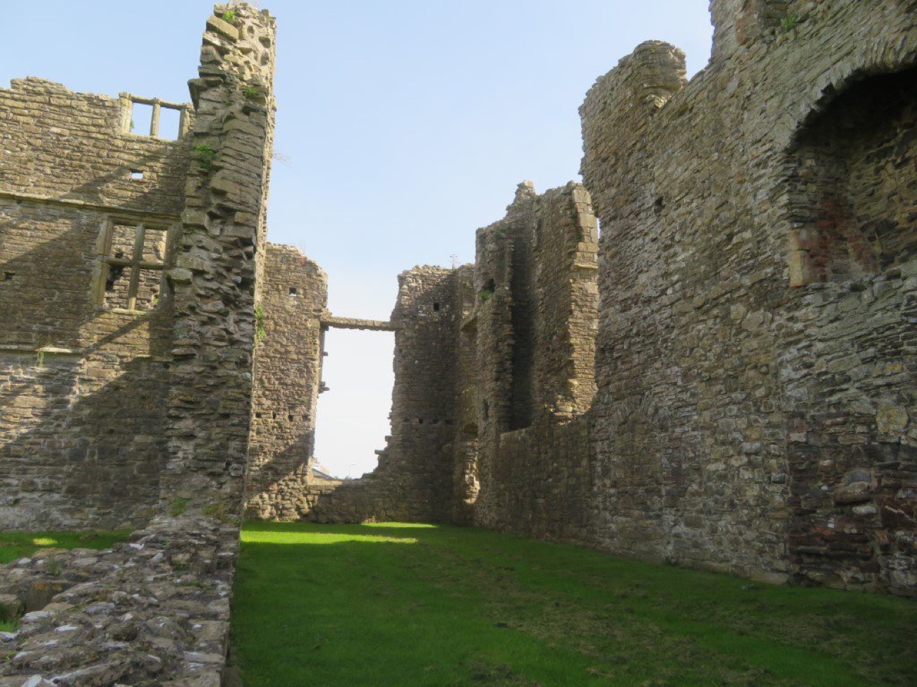 Inside the roofless ranges of Castle Caulfield, tall stone walls with window openings and a grass floor between them