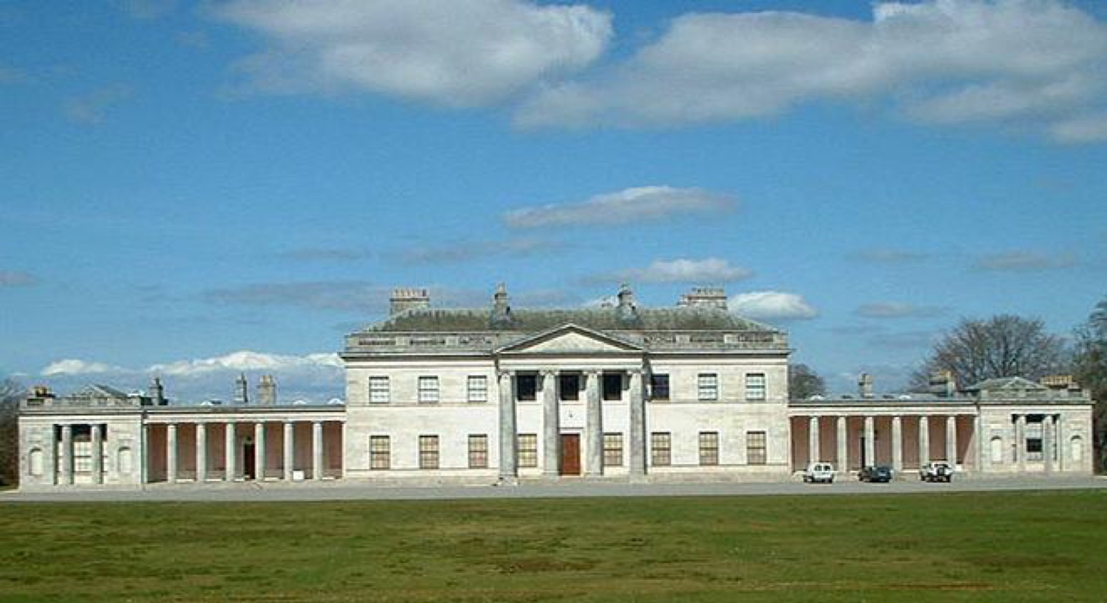 The long neoclassical Portland-stone facade of Castle Coole stretched across a green lawn under a blue sky