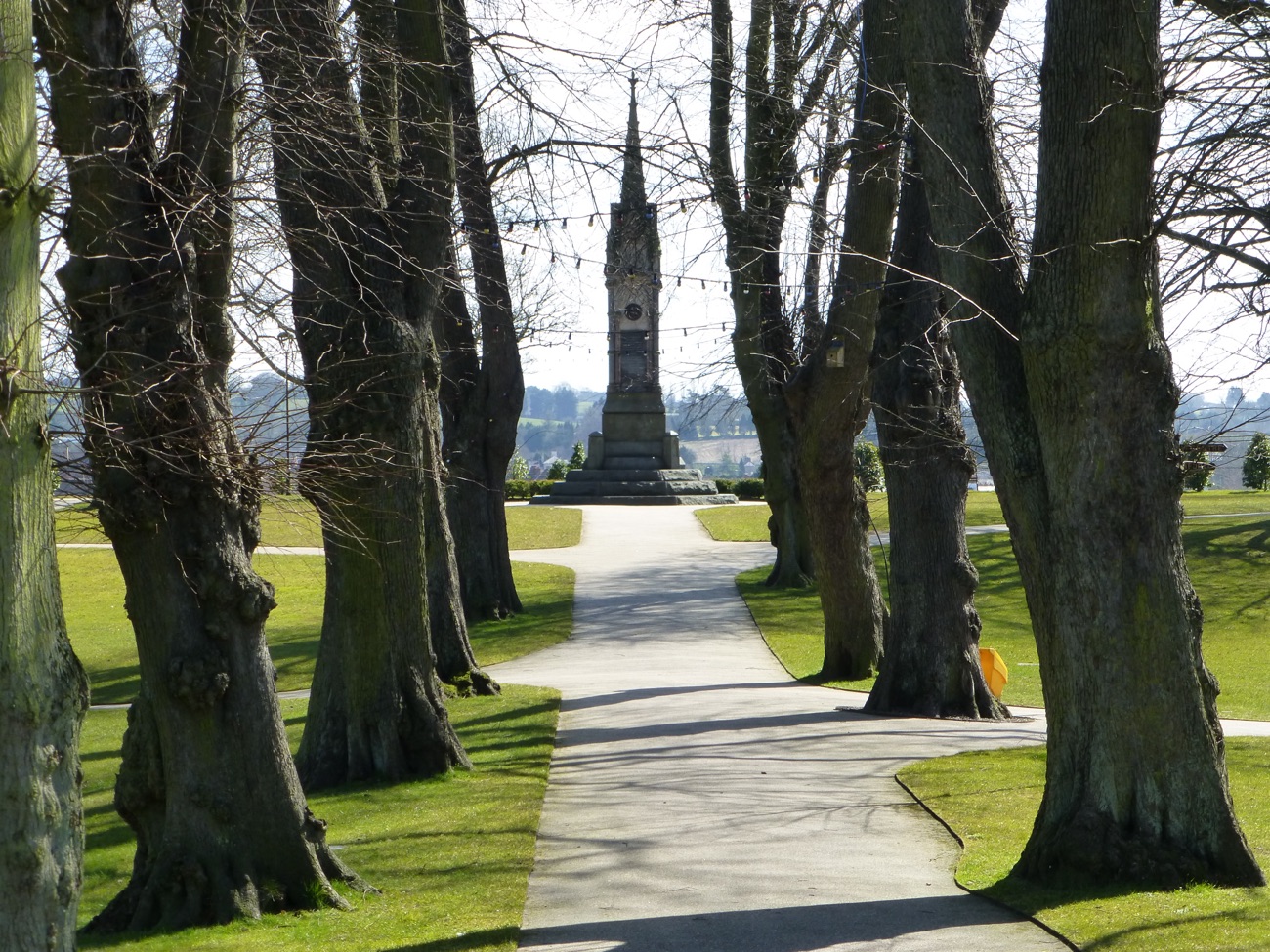 An avenue of tall trees at Castle Gardens leading towards a stone monument