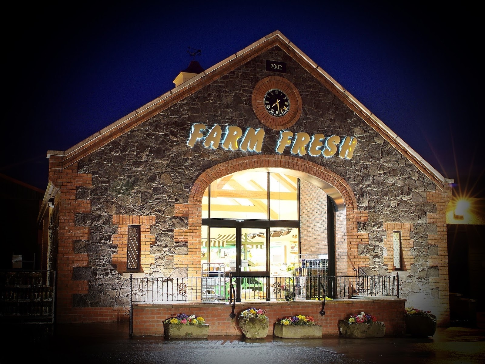 Chapman's Farm Fresh at dusk — a stone barn with a clock and FARM FRESH lit up across the gable
