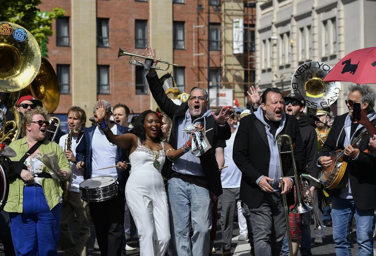 A jazz band with trumpets and saxophones performing outdoors to a smiling festival crowd in Derry