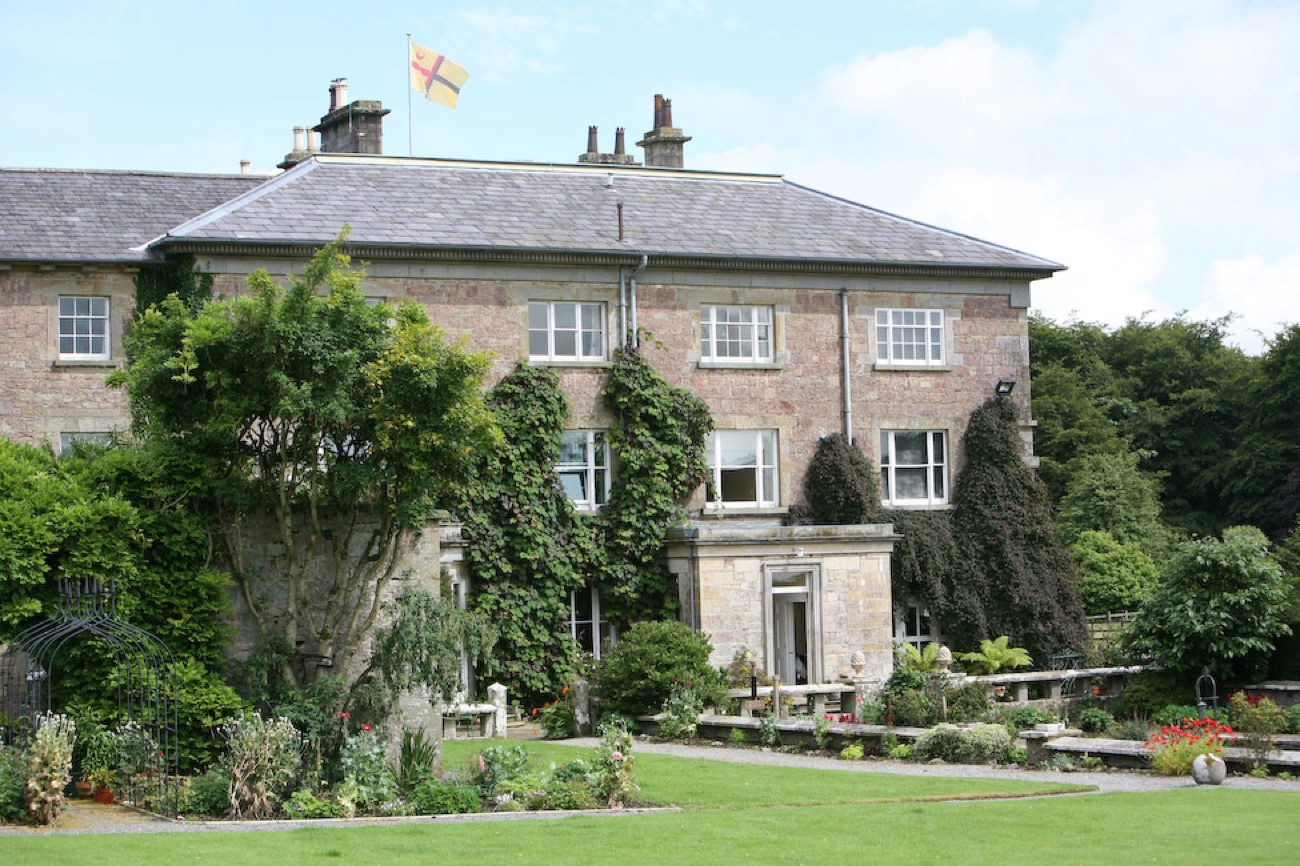 The garden front of Colebrooke Park, wisteria climbing the stone and a terraced flower garden with a metal pergola below