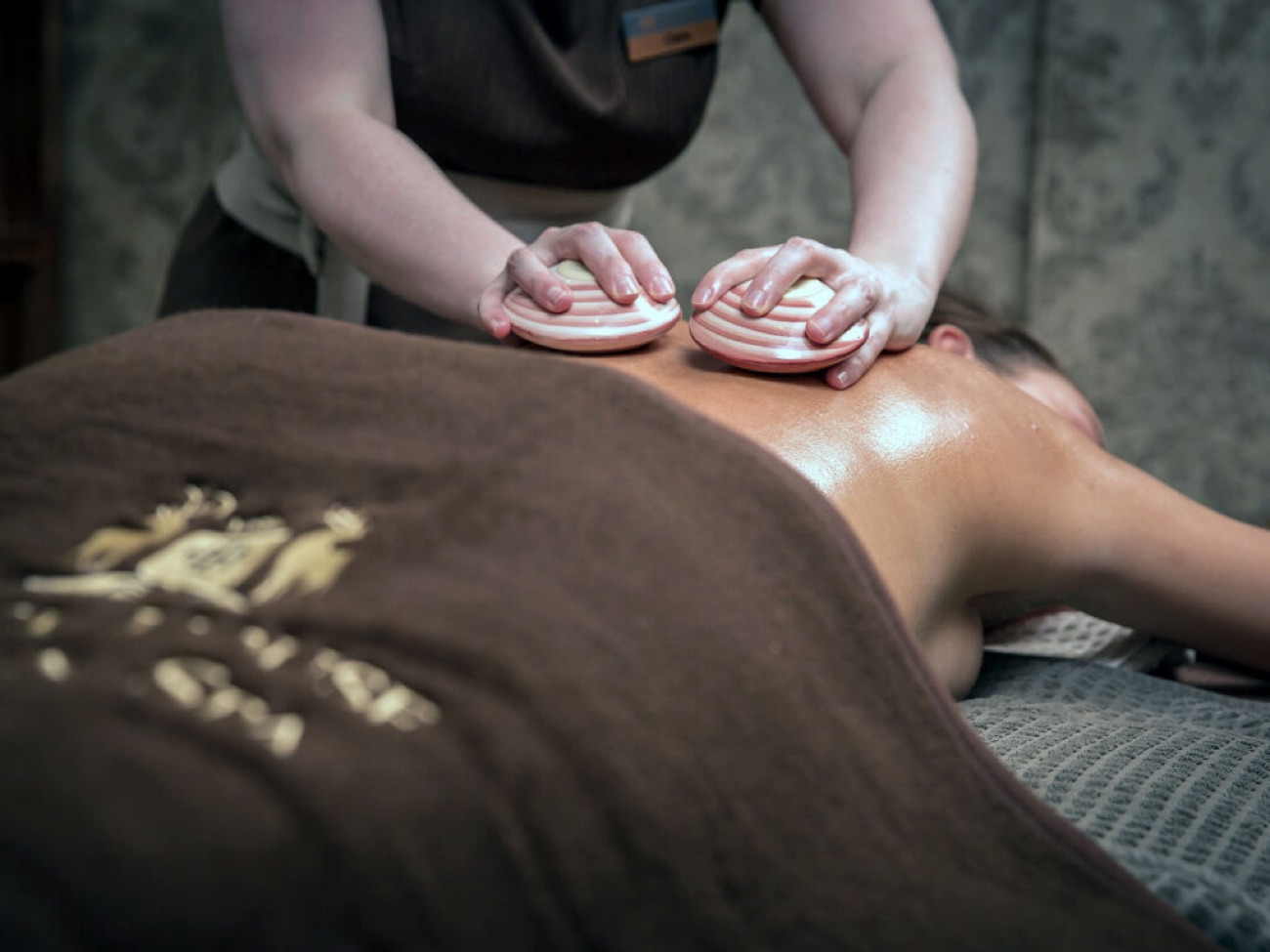 A therapist works through a warm-stone back treatment in a low-lit room.