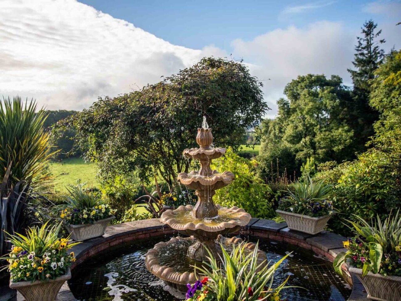 An ornamental fountain in the walled garden, open countryside beyond.