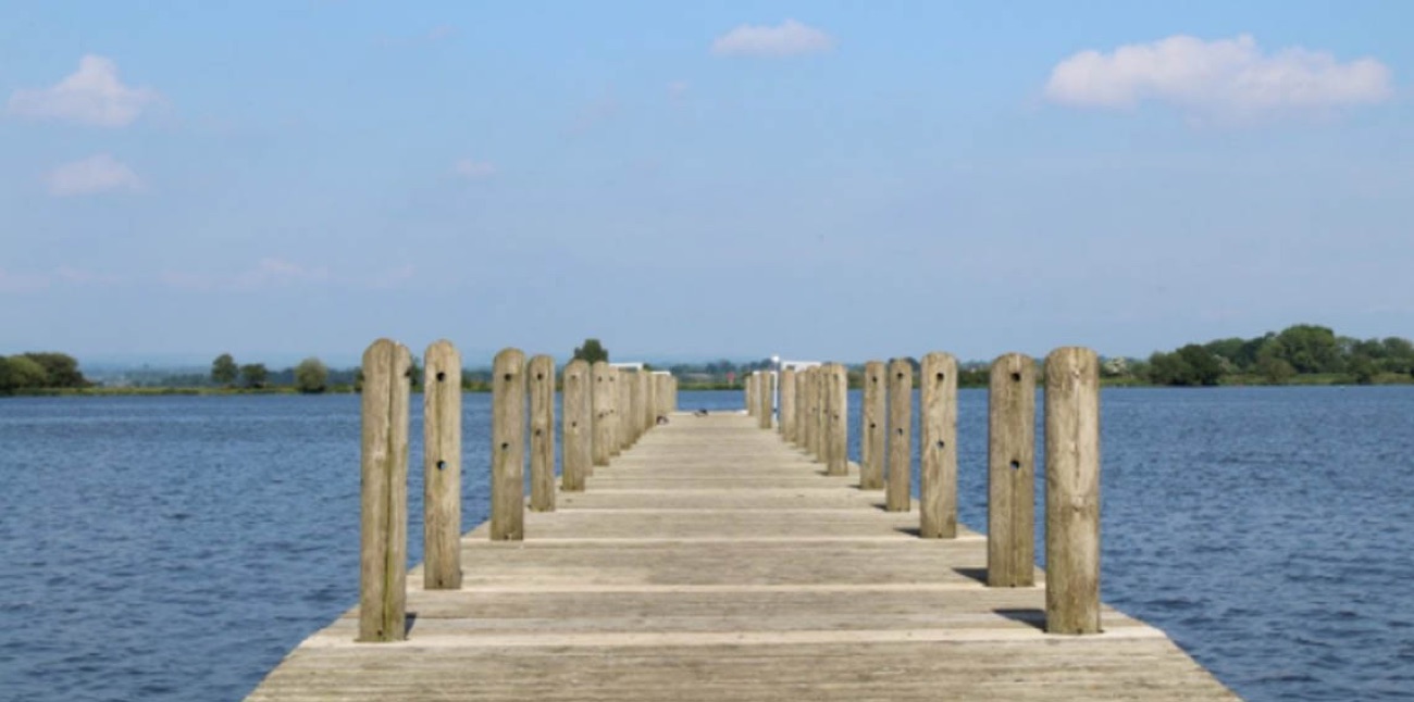 A wooden jetty running out over the still water of the lake under a blue sky